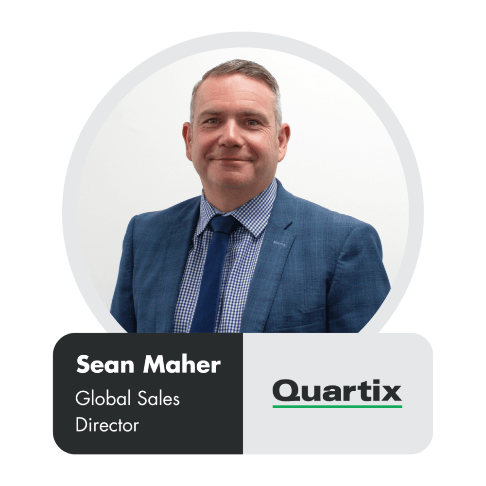 Man in a blue suit and checkered shirt smiles at the camera. Text reads: "Sean Maher, Global Sales Director, Quartix".