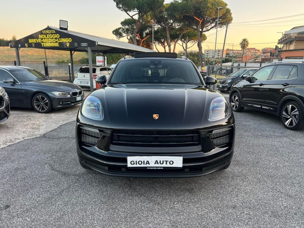 A black Porsche SUV is parked in a car lot, surrounded by other vehicles at Quartix Autosalone. The Gioia Srl dealership sign stands prominently in the background.