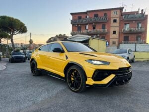 Un SUV giallo parcheggiato su una strada di fronte a una fila di edifici in mattoni, con auto e alberi sullo sfondo.