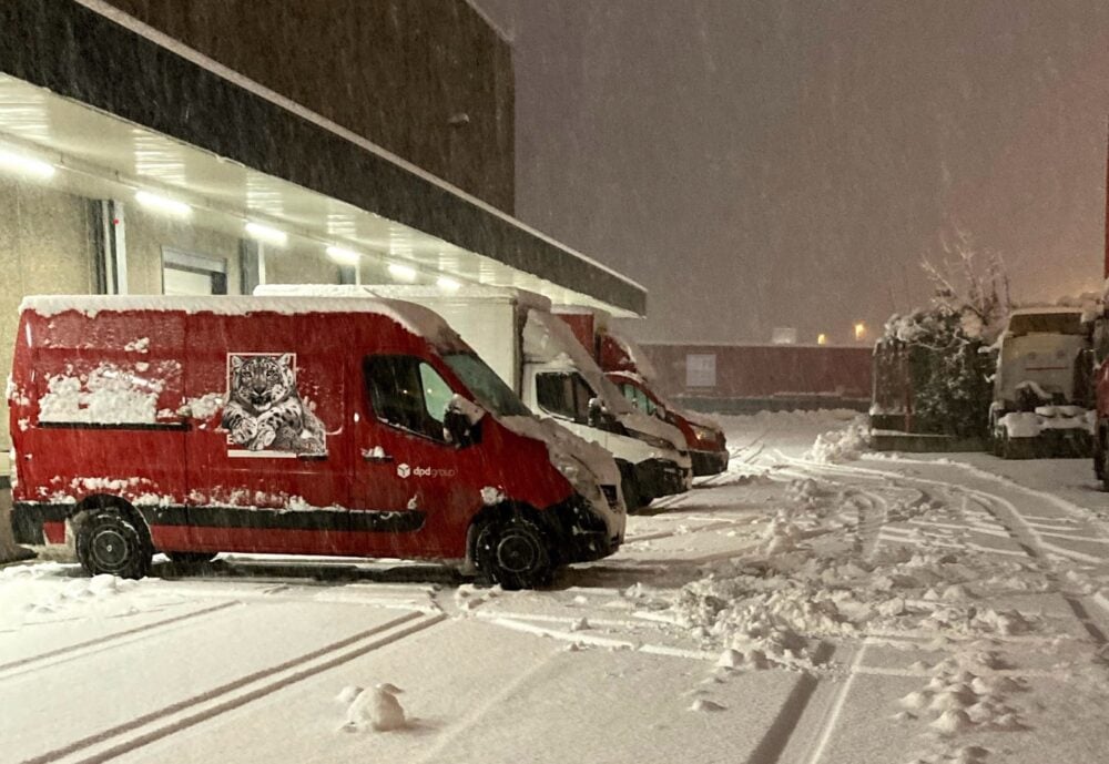 Red delivery vans parked in a snowy lot at night, with snow covering the ground and vehicles.