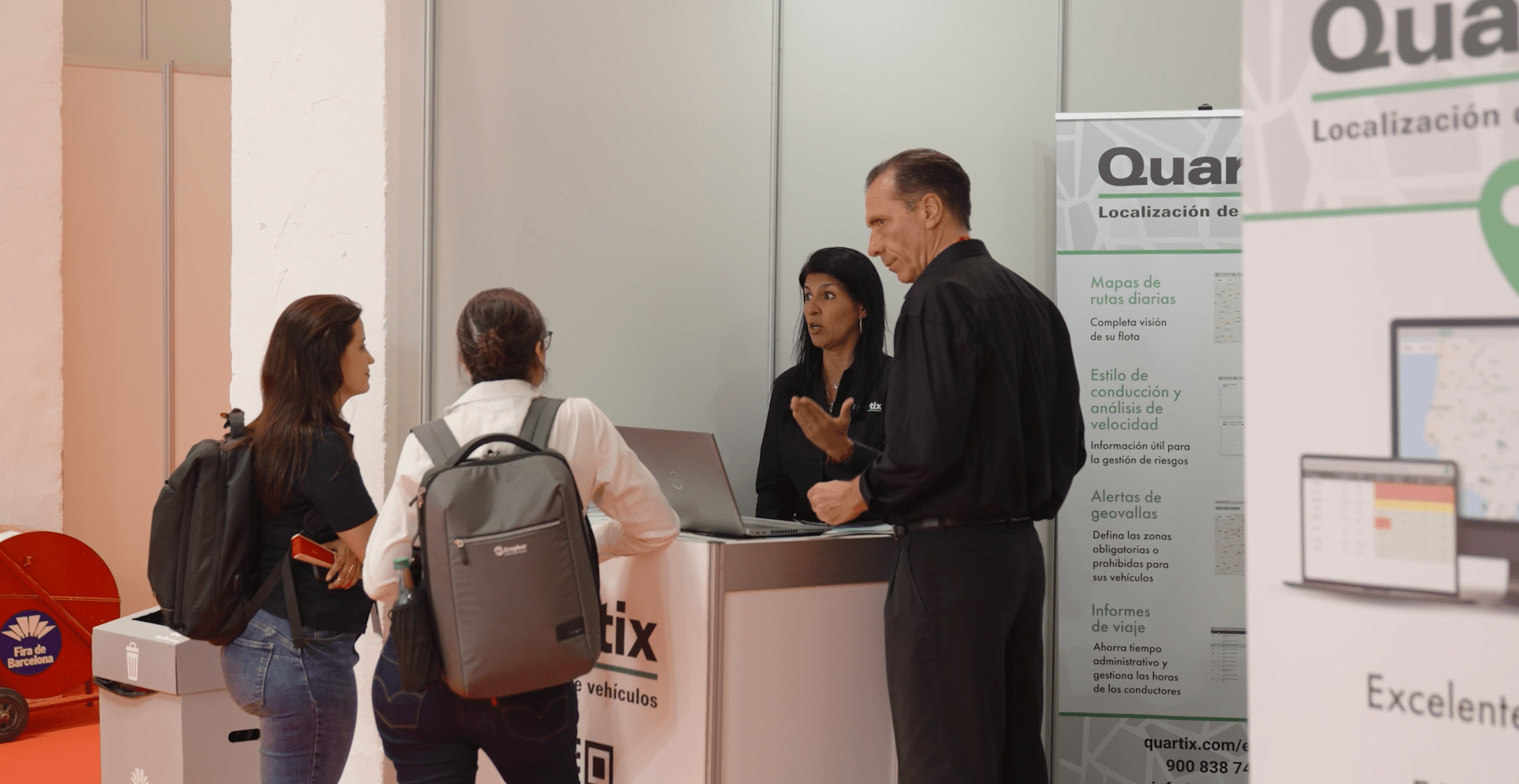 People at an exhibition booth discussing with two representatives. A banner with product information is next to them.