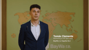 A man in a suit speaks in front of a world map backdrop. Text reads: "Tomás Clemente, Marketing & HR Specialist, BayWa r.e. España SLU.