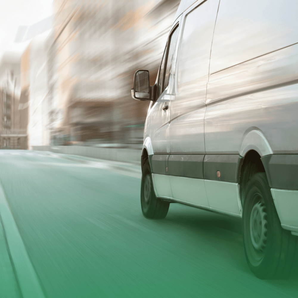 White delivery van in motion on a city street, with blurred buildings in the background.