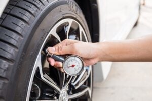 A person checks tire pressure with a handheld gauge on a car tire.