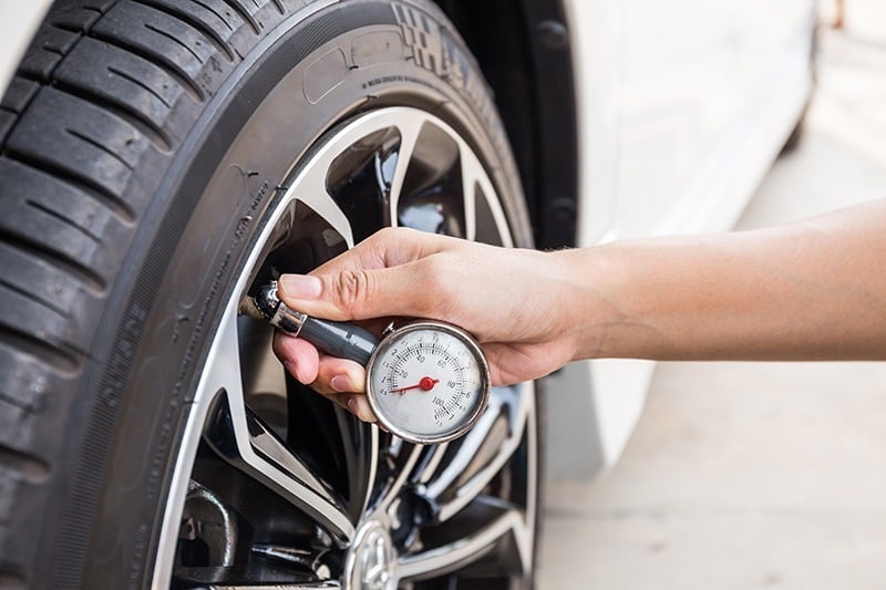 A person checks the air pressure of a car tire using a pressure gauge.