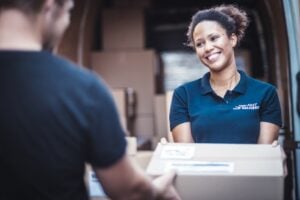 A delivery person hands a package to a customer in front of a van filled with boxes.