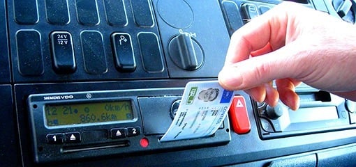 Hand inserting a card into a digital tachograph in a vehicle's dashboard.