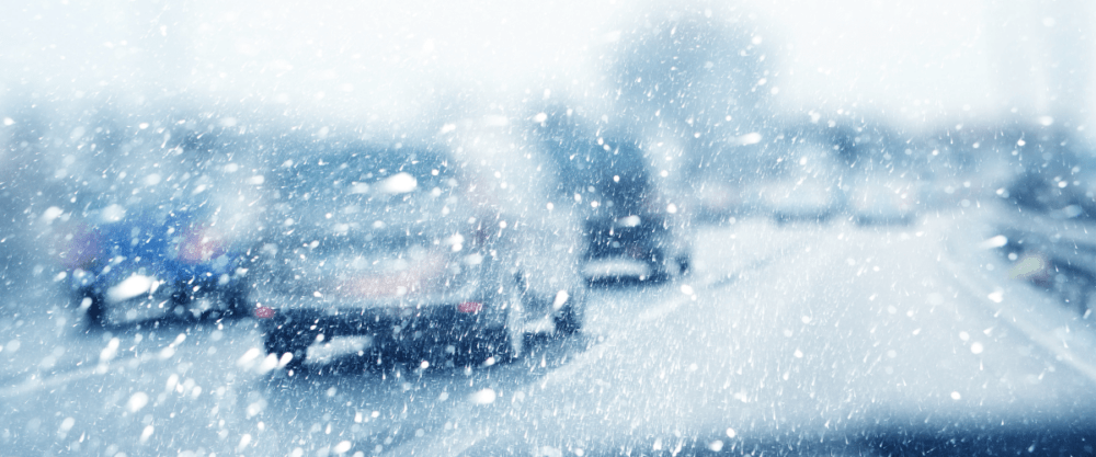 Cars navigating a snowy road amid heavily falling snow create a blurry, wintery atmosphere, showcasing the challenges of winter driving.