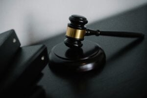 A wooden judge's gavel rests on a dark surface beside two black binders.