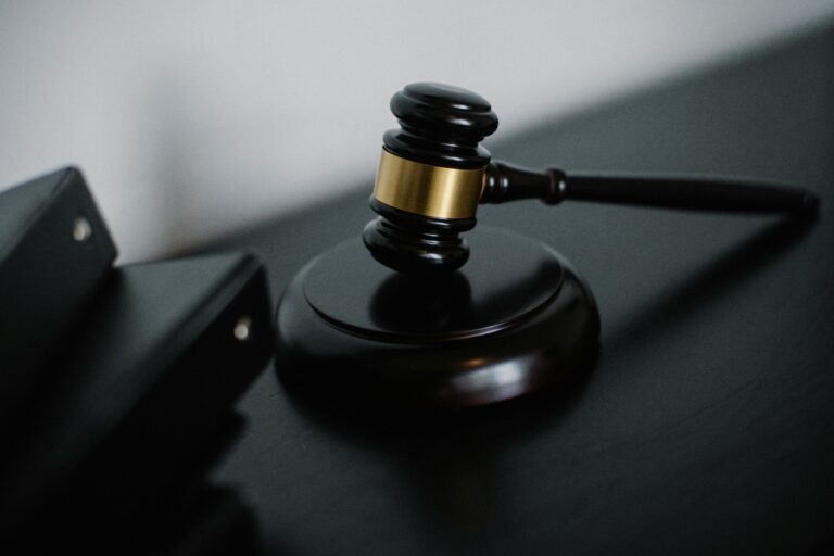 A wooden judge's gavel rests on a dark surface beside two black binders.